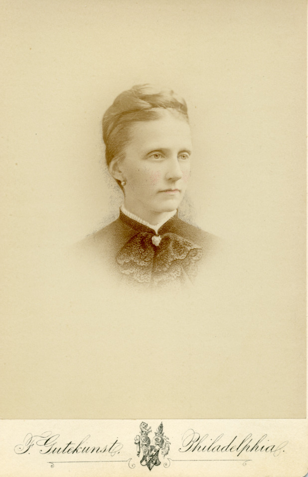 A yellowed bust photograph of Emma Bouvier Drexel. She is facing away from the camera and is wearing a high collar, pearl earrings, and her light colored hair is pinned up.