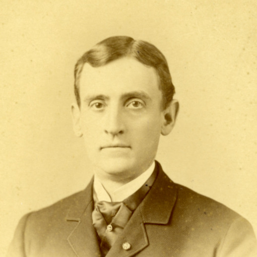A yellowed photograph of Walter G Smith. He is wearing a suit jacket over a white collared shirt and scarf. His hair is slicked back and he is facing the camera.