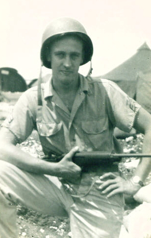 Out of focus photograph of Bob Ong in WWII uniform with short sleeves, and he's wearing a helmet and carrying a gun in front of an Army tent.