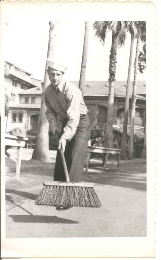 Coast Guardsman with a large broom in his hand with the Hotel Ponce de Leon behind him