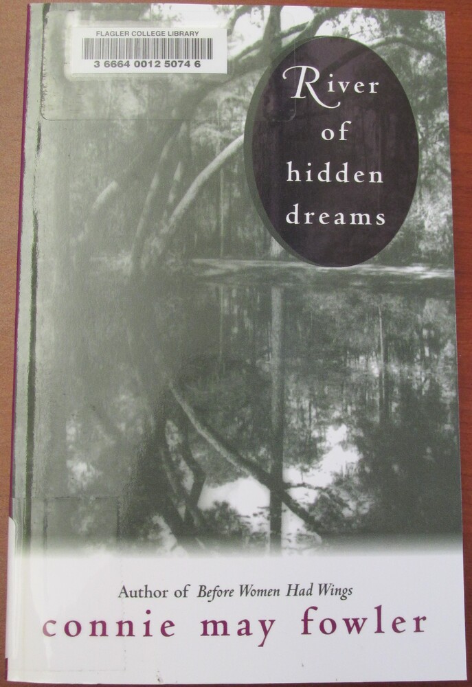 This book is titled "River of Hidden Dreams" by Connie May Fowler. The cover of the book contains a black and white photograph of a swamp. The water reflects the trees and the Spanish moss above it. The title is on the upper right hand side of the book cover in a purple circle.