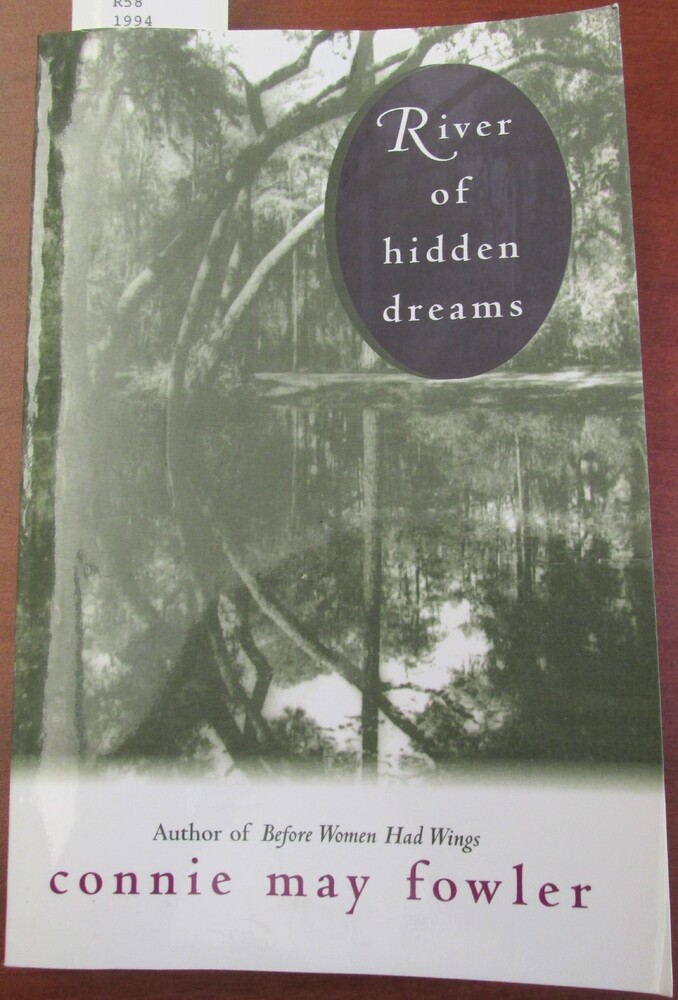 This book is titled "River of Hidden Dreams" by Connie May Fowler. The cover of the book contains a black and white photograph of a swamp. The water reflects the trees and the Spanish moss above it. The title is on the upper right hand side of the book cover in a purple circle.