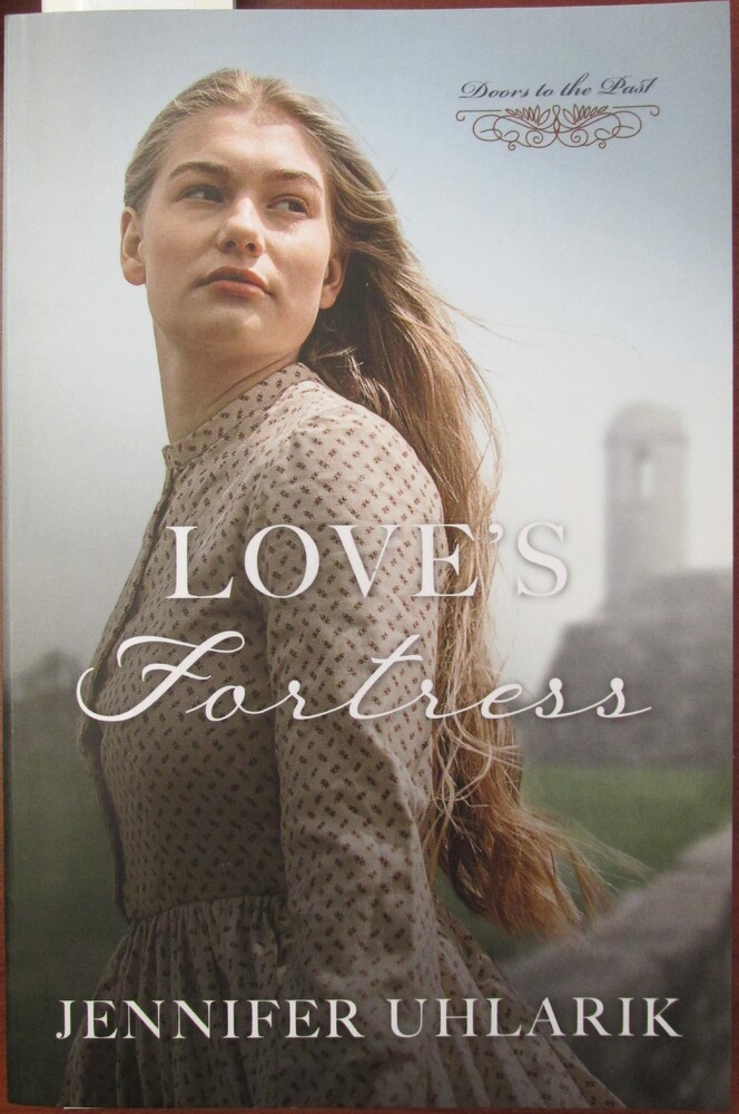 This book is titled "Love's Fortress" by Jennifer Uhlarik. The book cover includes a photograph of a young woman in period dress. Her hair is long and light brown and she looks behind her. The Castillo de San Marcos is in the background.