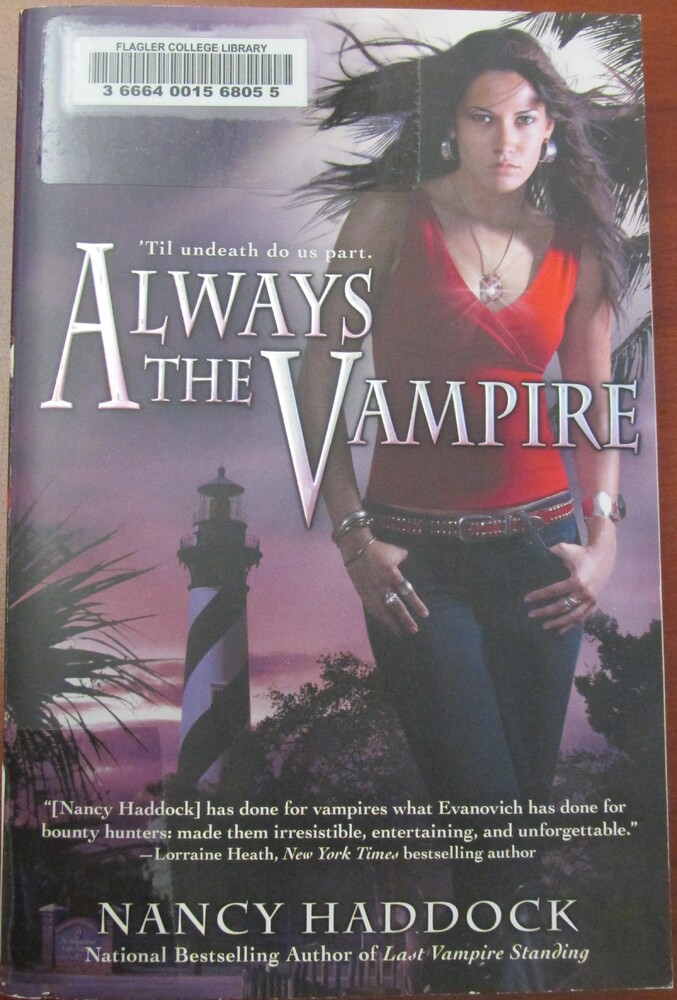 This book is titled "Always a Vampire" written by Nancy Haddock. The cover includes the tagline, "'Til undeath do us part." The cover showcases a young woman in dark jeans and a red tank top, with a glimmering necklace. Her hands, with many bracelets and rings, are in her pockets. Behind her is the St. Augustine lighthouse.