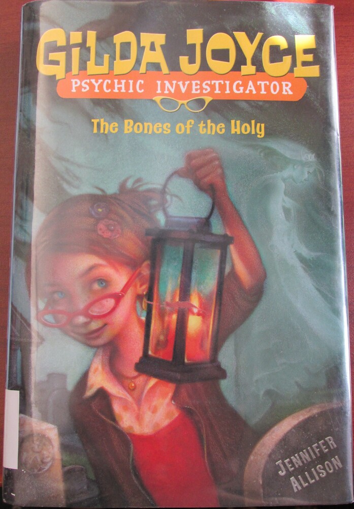 This book is titled "The Bones of the Holy" written by Jennifer Allison. The cover of this book features a young red-head woman with bright blue eyes and red glasses lowered to her nose. She is holding a burning lantern and looks around her surroundings. She is standing in a cemetery. The ghost of a woman in a crown stands to her right.