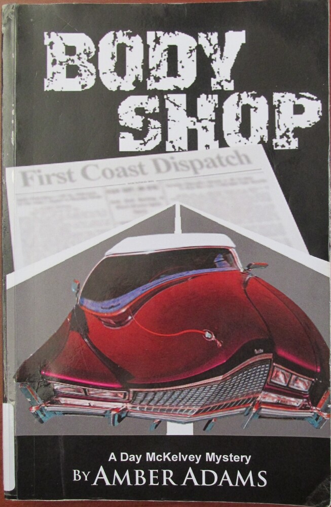 This book is titled "Body Shop" or "A Day McKelvey Mystery, Book 3" by Amber Adams. The cover of this book has a black background and an up close of a classic red car with a curved hood. The car is driving over a gray street, positioned over a newspaper titled "First Coast Dispatch."