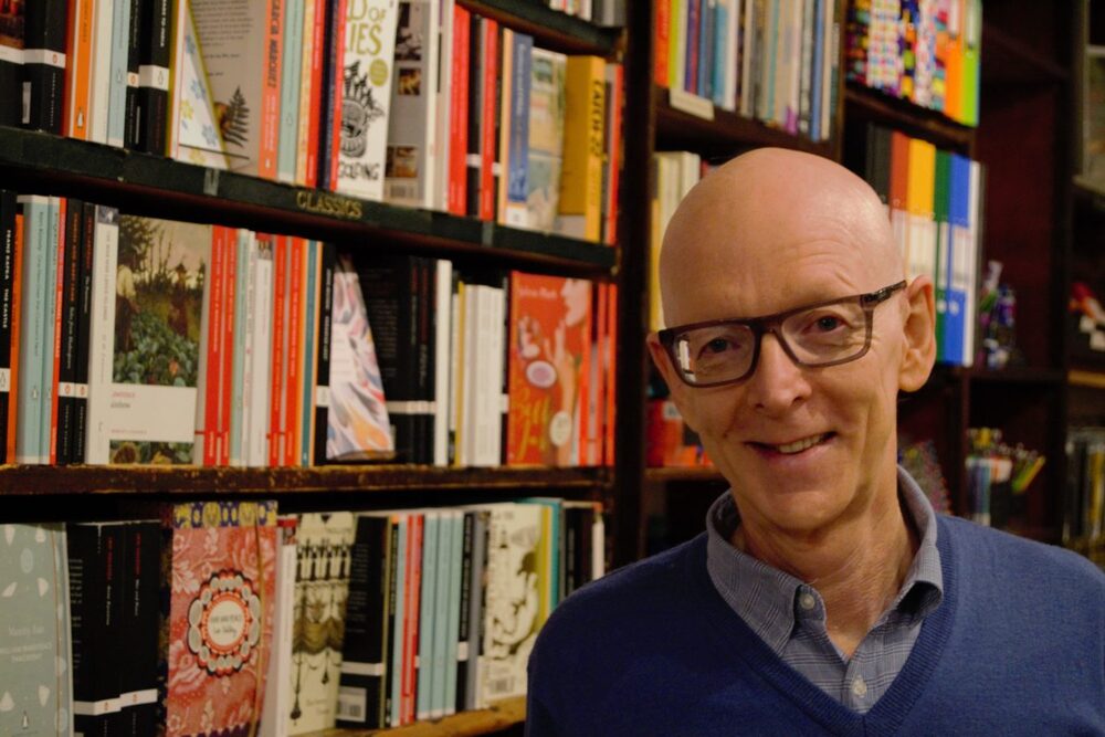 A colour photograph of a man in front of bookshelves