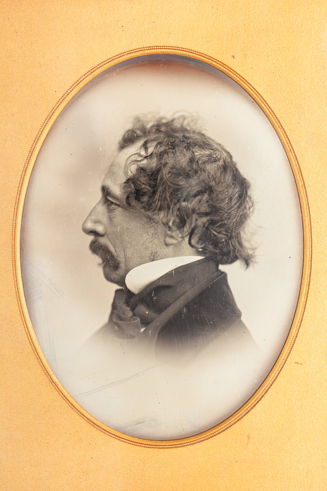 A side profile black and white image of a middle-aged man in an oval mount. His dark hair is swept forwards curling at the temples and a thick dark moustache curves down towards his jawline. A collar, voluminous neckties and collared jacket cover his throat and neck.